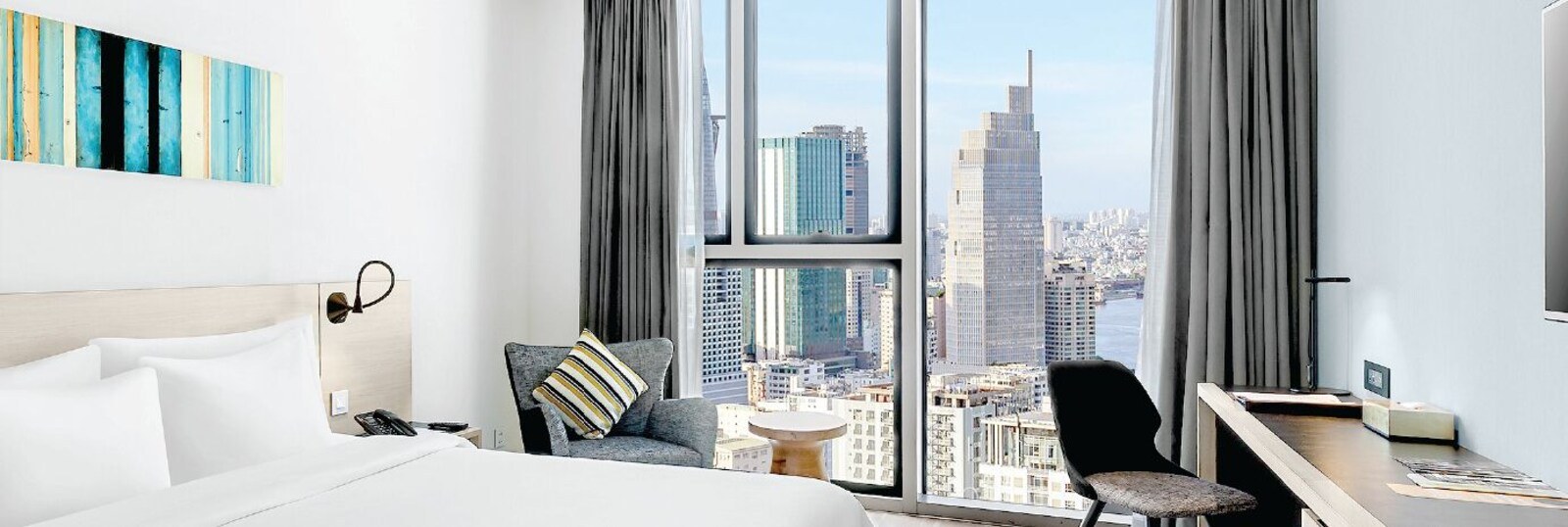 A hotel room with a large bed, a desk, a chair, and a view of a cityscape through large windows. - Liberty Central Saigon Citypoint (Ho Chi Minh City)