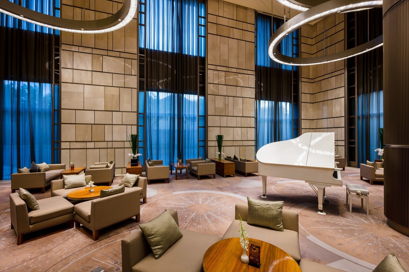 A spacious lobby with a grand piano, comfortable seating, and a large window with blue curtains. - Hotel Nikko Saigon (Ho Chi Minh City)