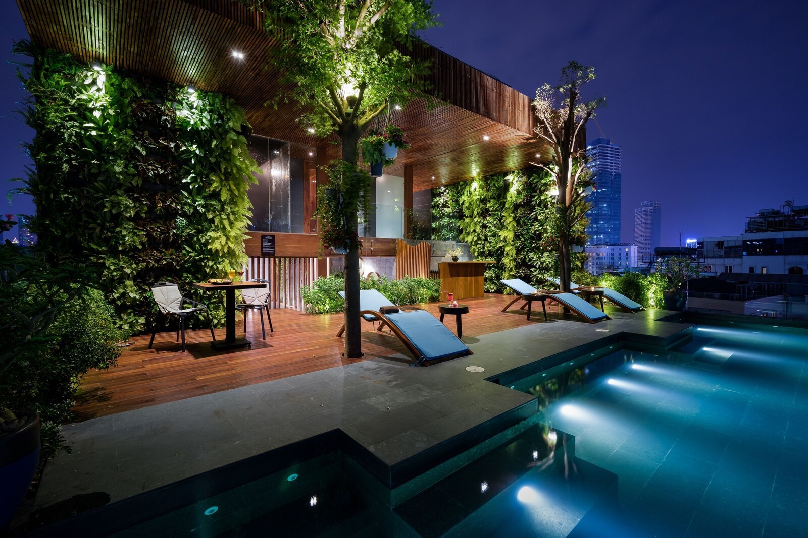 A rooftop pool area with lounge chairs and a wooden deck, surrounded by lush greenery and modern architecture. - Silverland Yen Hotel (Ho Chi Minh City)